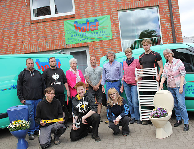 Gruppe von Personen vor grünem Transporter und Backstein-Gebäude.