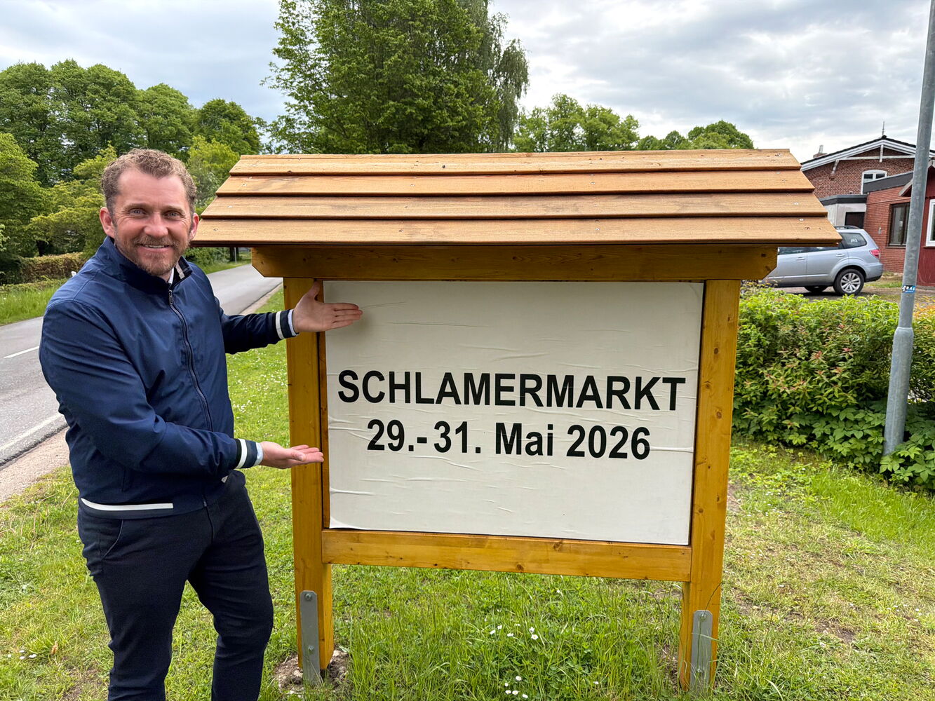 Mann zeigt auf Schild mit Schriftzug 'Schlamermarkt 29.-31. Mai 2026'