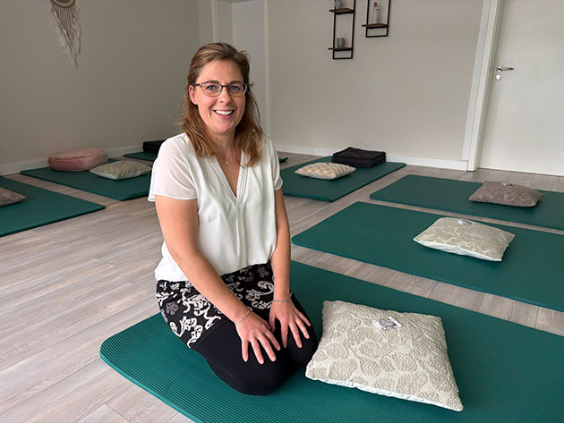 Frau sitzt lächelnd auf Matte in hellem Yogaraum.