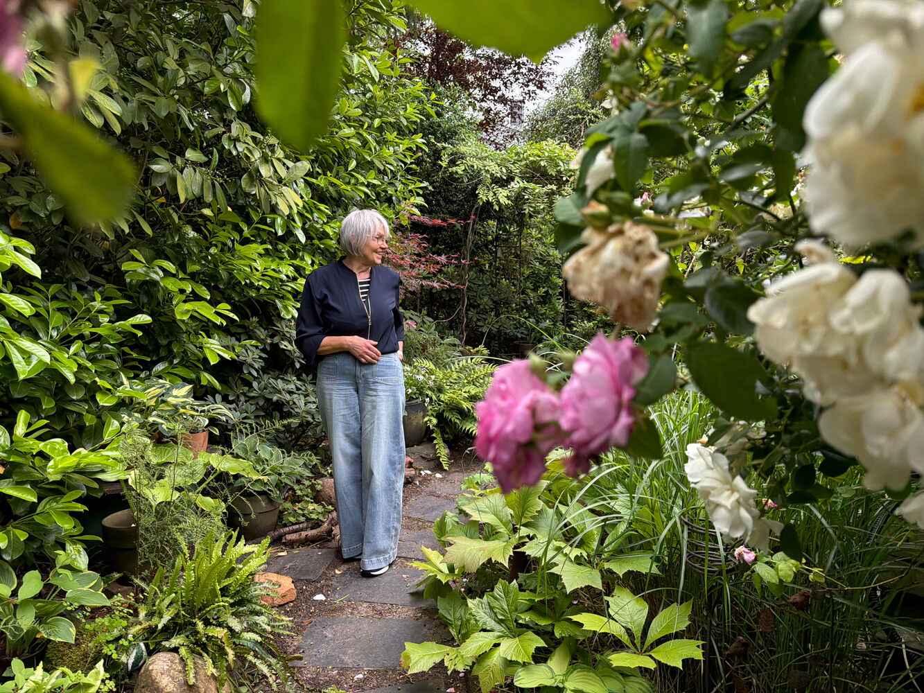 Frau im Garten umgeben von grünen Pflanzen und Blumen.