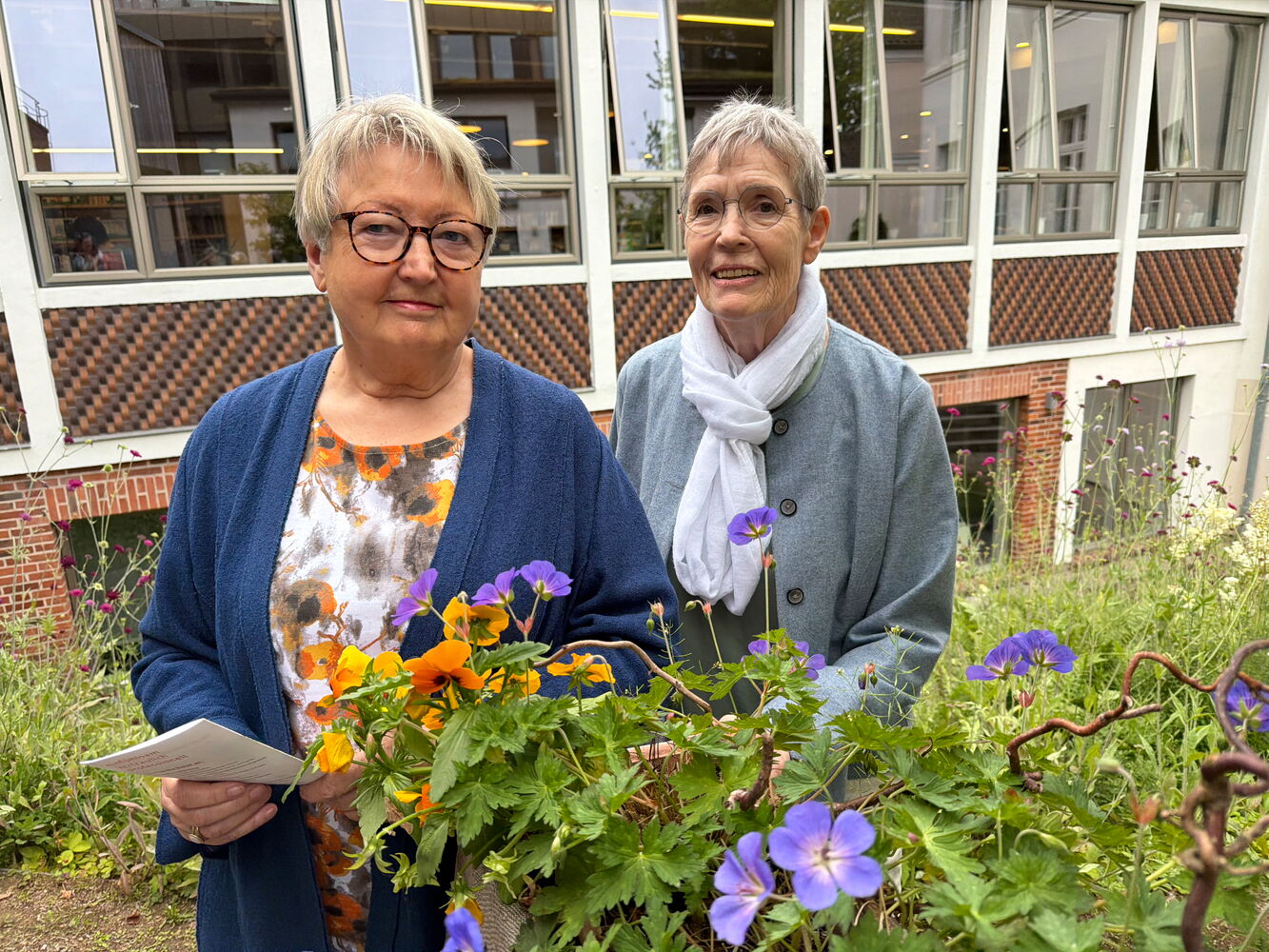 Zwei Frauen mit Blumen vor einem Gebäude.