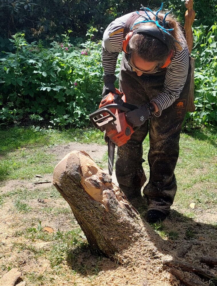 Person schnitzt mit Motorsäge an Baumstamm im Garten.