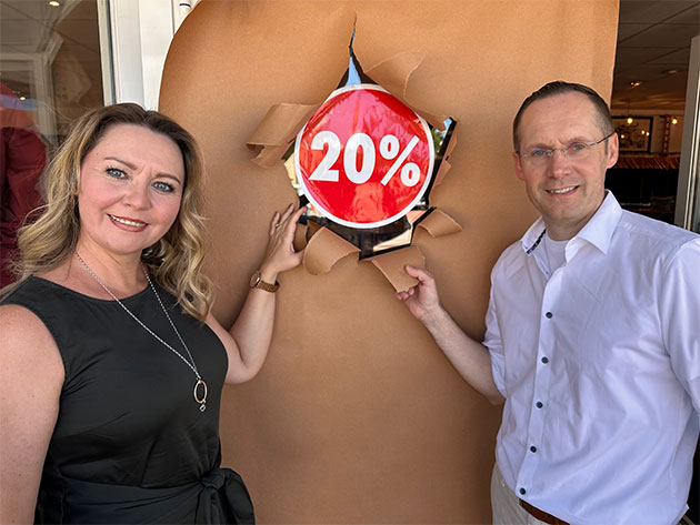 Zwei Personen neben 20%-Rabatt-Schild im Geschäftseingang.