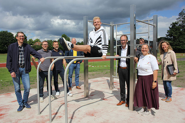 Gruppe posiert an Außensportanlage bei bewölktem Himmel.