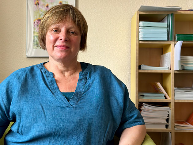 Frau in blauem Hemd sitzt vor einem Regal mit Büchern.