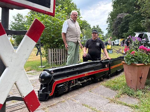 Zwei Männer mit einer Miniatureisenbahn im Garten.