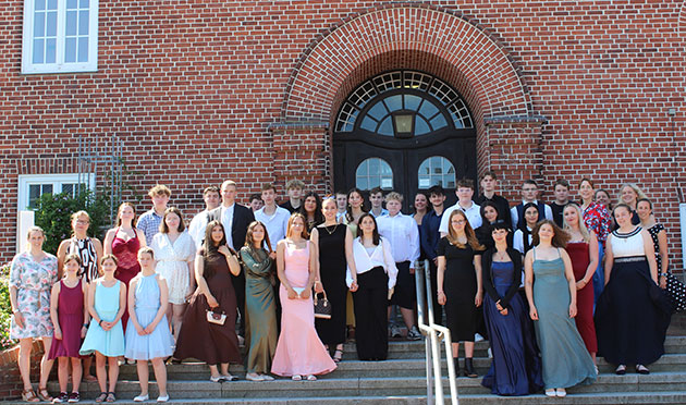 Große Gruppe junger Leute in formeller Kleidung vor Backsteingebäude.