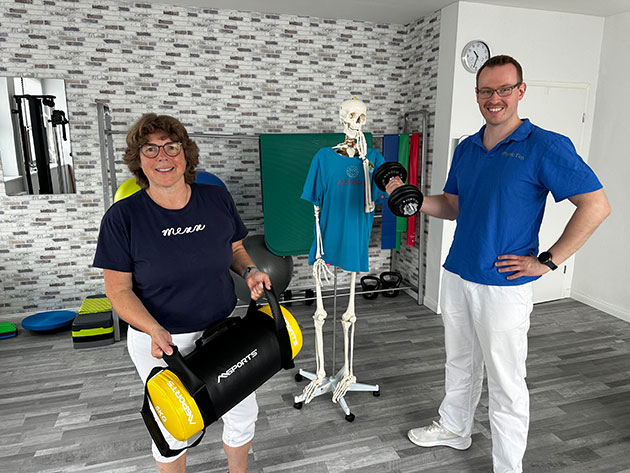 Zwei Personen mit Hanteln vor einem Skelett in einem Fitnessraum.
