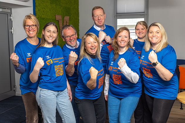 Gruppe von acht Personen in blauen T-Shirts posiert lächelnd.