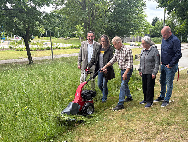 Fünf Personen schauen eine rote Maschine im Gras an.