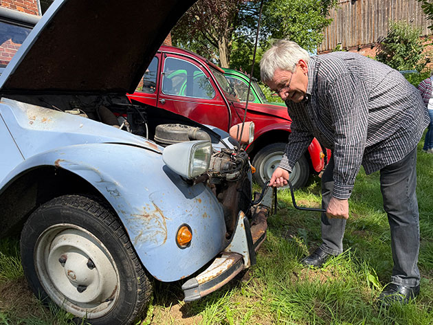 Mann startet blauen Oldtimer mit Kurbel bei Sonnenschein.
