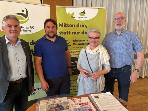 Vier Personen vor zwei Info-Ständen in einem Raum.