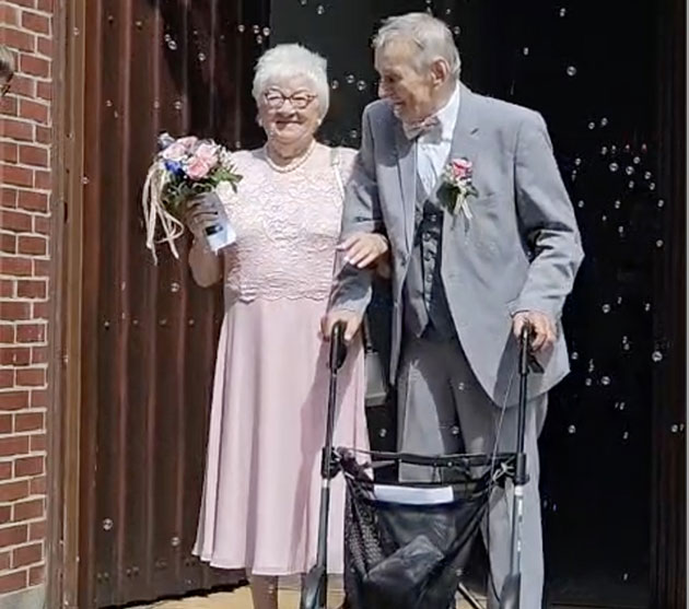 Älteres Paar verlässt die Kirche mit Blumen und Rollator.