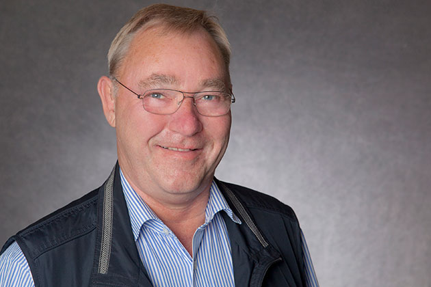 Mann mit Brille und Weste lächelt vor grauem Hintergrund.