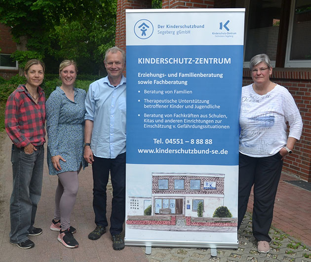 Vier Personen stehen neben einem Kinderschutz-Banner.