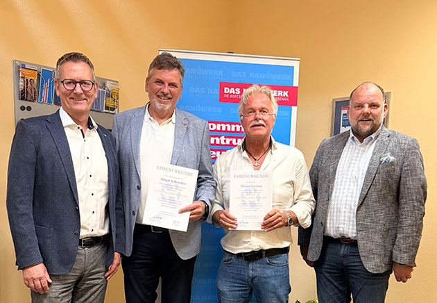 Vier Männer posieren mit Urkunden vor einem Banner.