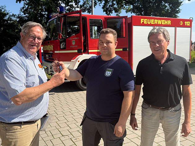 Drei Männer vor einem Feuerwehrfahrzeug bei der Schlüsselübergabe