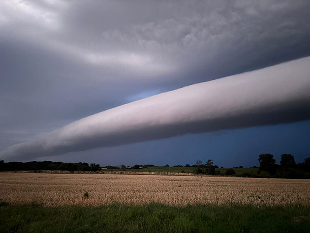 Langer Wolkenstreifen am Himmel über einem Feld bei Gewitter.