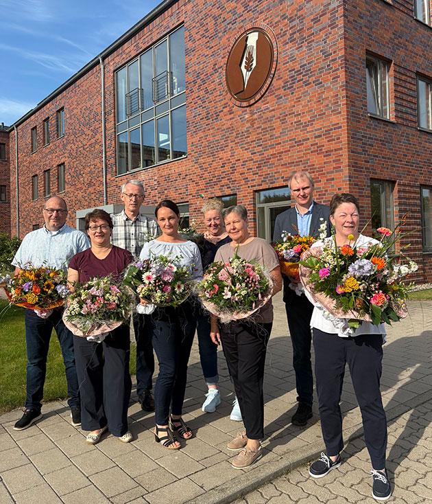 Gruppe von Menschen mit Blumensträußen vor einem Backsteingebäude.
