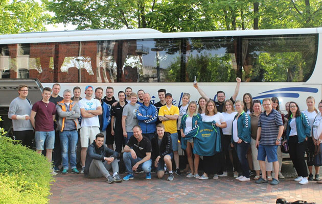 Gruppe posiert vor Reisebus im Grünen.