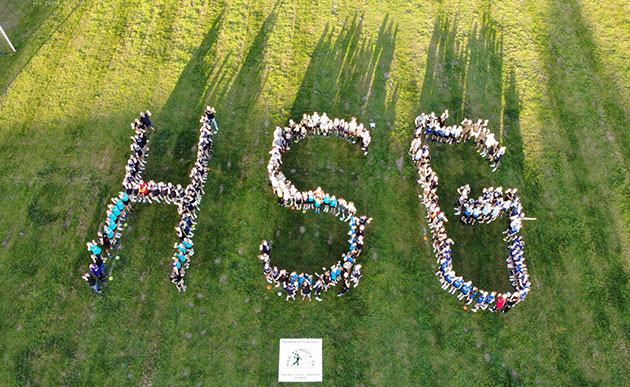 Luftaufnahme von Menschen formt "HSG" auf Wiese.