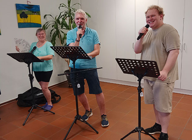 Drei Personen singen mit Mikrofonen und Notenständern.