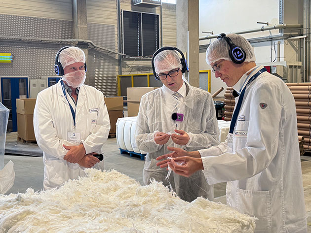 Drei Männer in Laboranzügen untersuchen Material im Labor.
