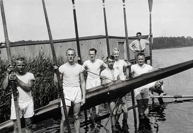 Ruderteam posiert mit Boot am Seeufer.