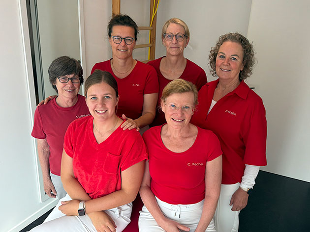 Sechs Frauen in roter Kleidung lächeln in die Kamera.