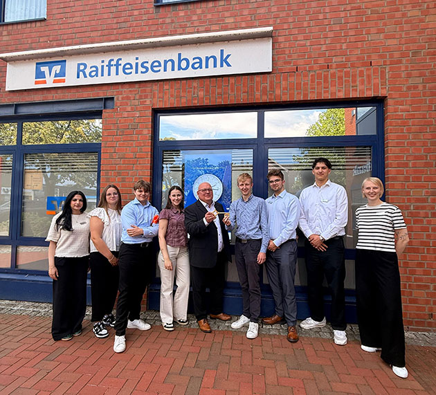 Gruppe vor einer Raiffeisenbank-Filiale posiert lächelnd.