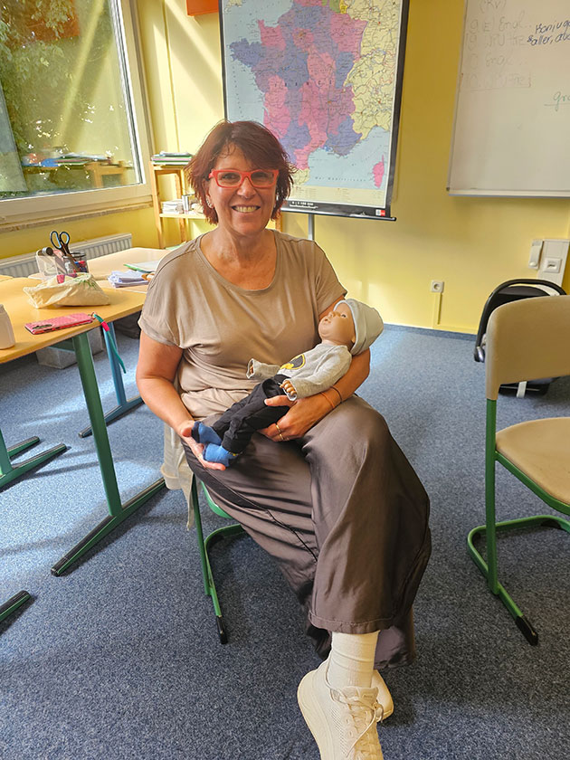 Frau hält Puppe in einem Klassenzimmer mit Frankreichkarte.