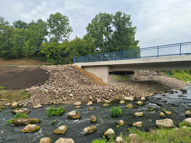Brücke über Bach mit Felsen und Pflanzen im Wasser.