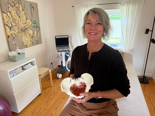 Frau mit anatomischem Beckenmodell in Behandlungszimmer.