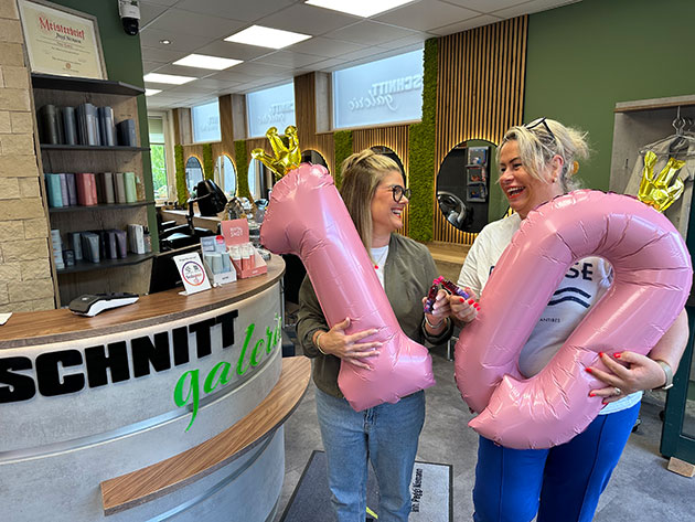 Zwei Frauen halten rosa Luftballons mit der Zahl 10 in einem Salon.