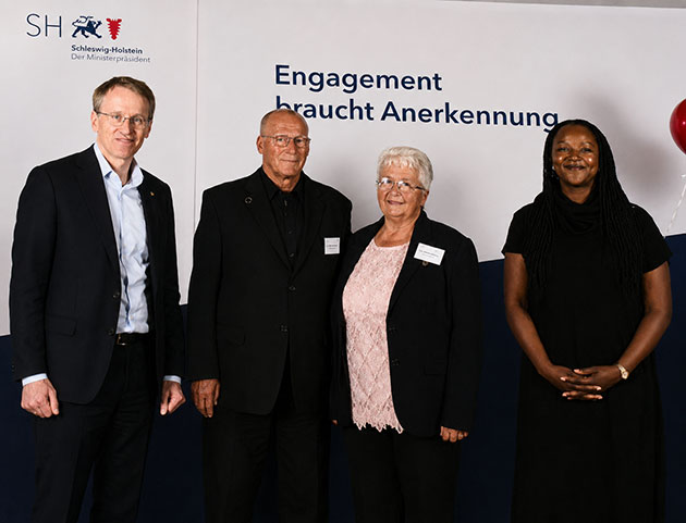Vier Personen vor einem Schild mit Text.