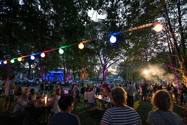 Menschen feiern bei einem bunten Fest im Park am Abend.