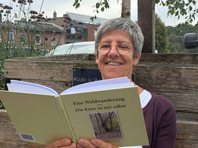 Frau liest Buch auf einer Bank im Freien.