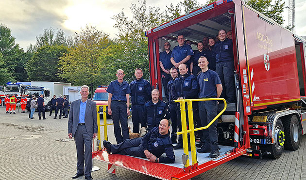 Gruppe von Feuerwehrleuten posiert auf Einsatzfahrzeug.