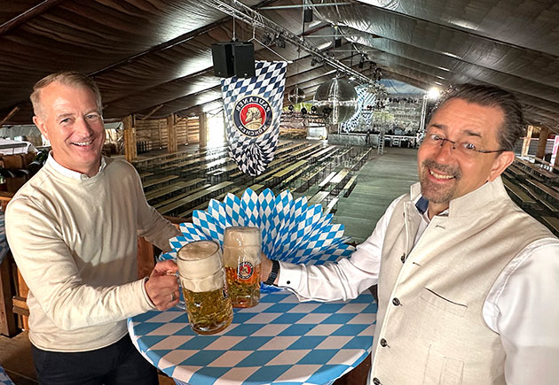 Zwei Männer mit Bierkrügen im leeren Festzelt.