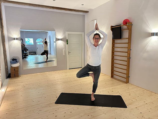 Frau in Yoga-Pose auf Matte in hellem Raum mit Spiegel.