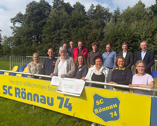 Gruppe posiert mit Scheck vor SC Rönnau 74 Schild.