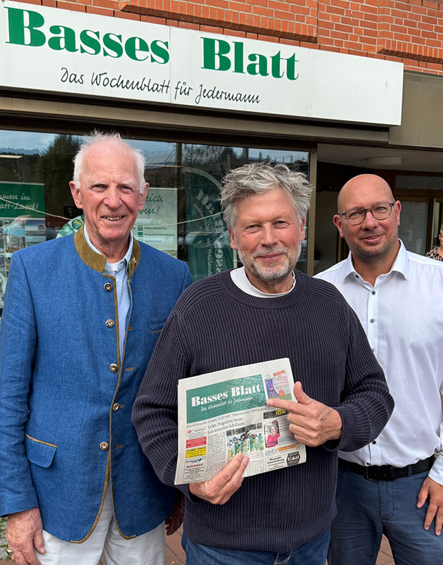 Drei Männer vor Basses Blatt Büro, einer hält Zeitung.
