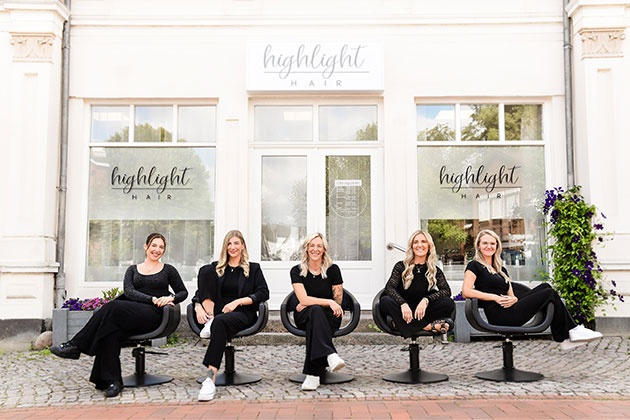 Fünf Frauen sitzen vor einem Friseursalon auf Drehstühlen.