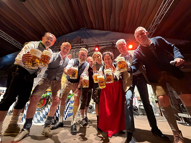 Gruppe in Tracht mit Bierkrügen auf der Bühne.
