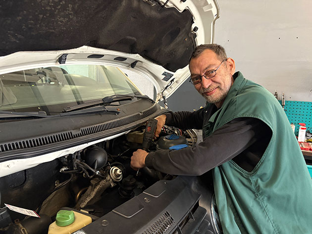 Mechaniker arbeitet lächelnd am Motor eines Fahrzeugs.