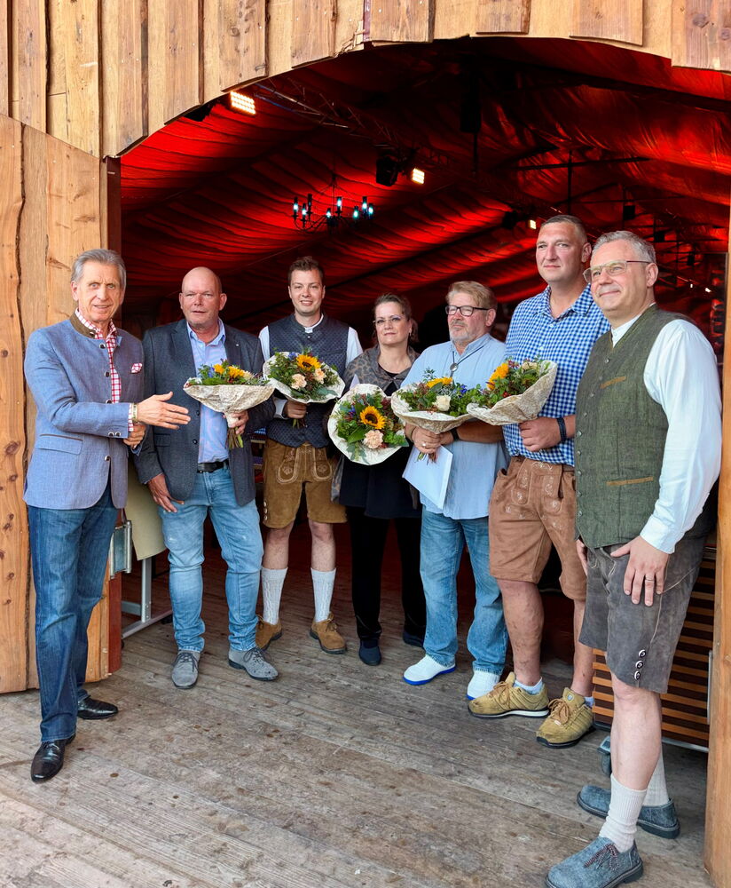 Gruppe von Menschen mit Blumensträußen vor Holzhütte.