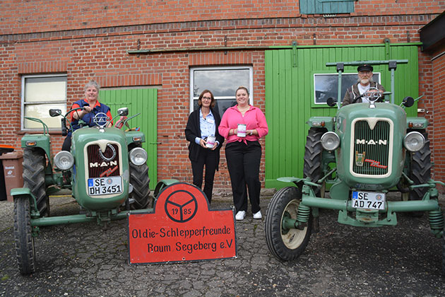 Personen posieren mit Oldtimer-Traktoren vor Ziegelwand.
