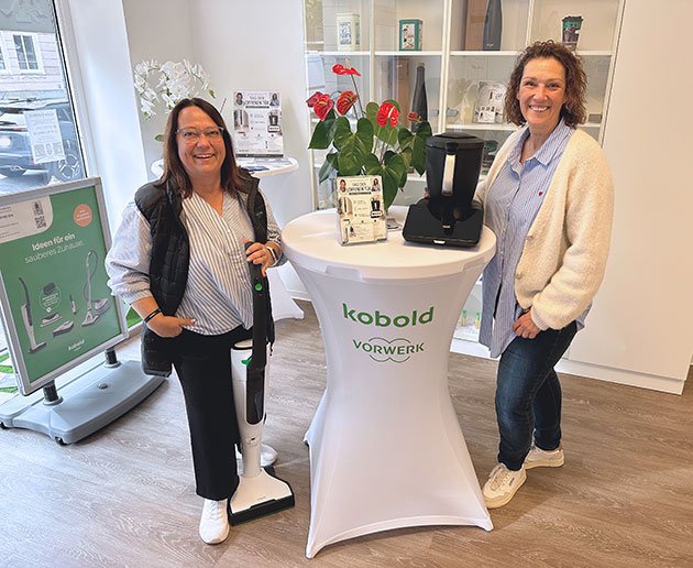 Zwei Frauen im Vorwerk-Geschäft neben einem Tisch mit Geräten.