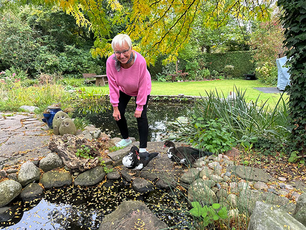 Frau füttert Enten an einem Teich im Garten.