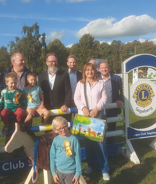 Gruppe von Menschen posiert vor Lions Club Schild im Freien.